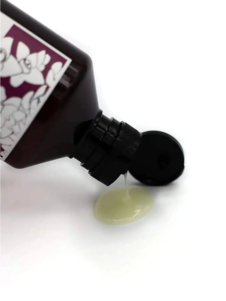 A clear, light green liquid pours out from the open cap of a Davines REPLUMPING Shampoo bottle onto a white surface | Twentyseven Toronto