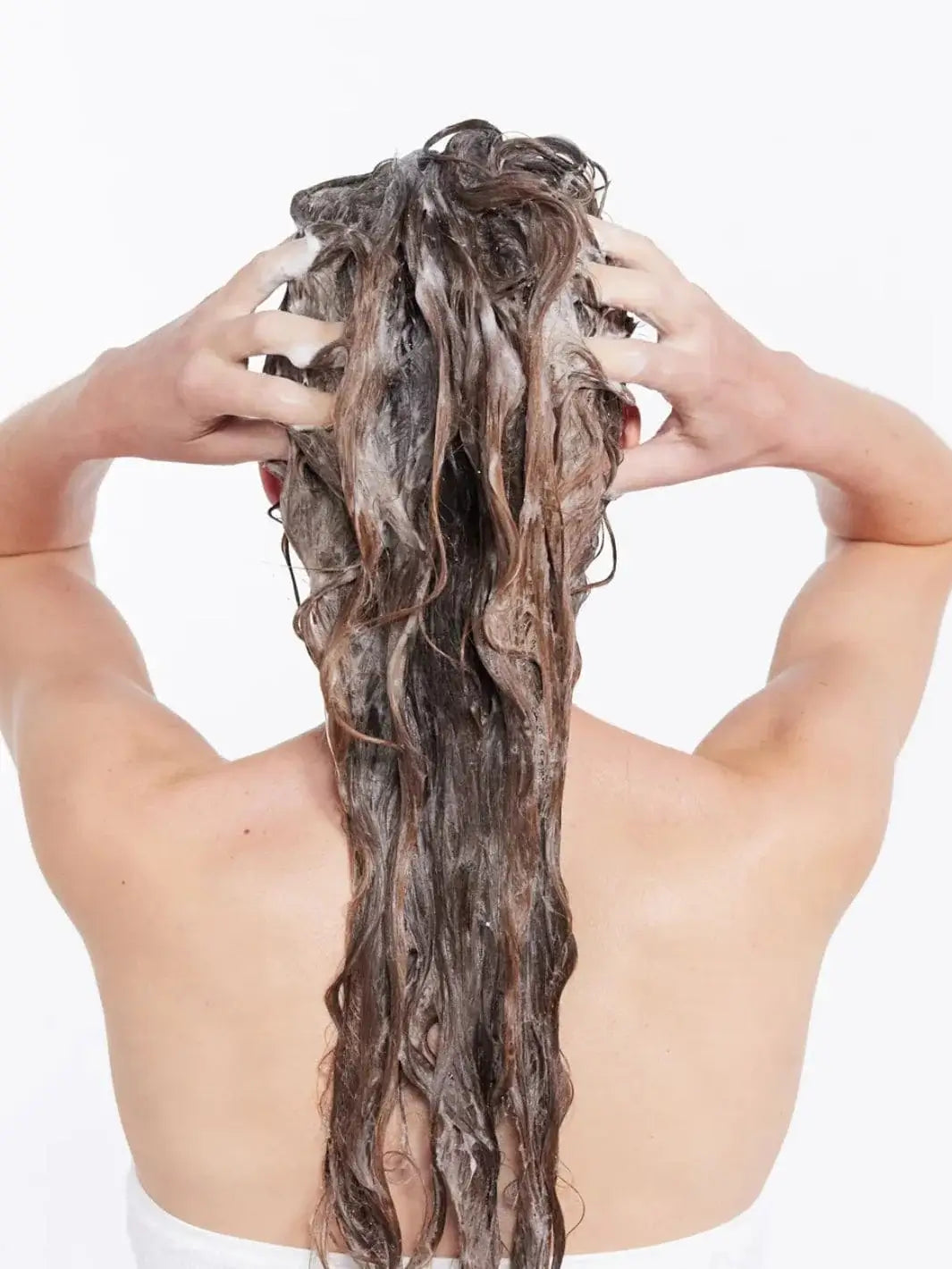 A back view shows a person massaging a rich lather into their long, wet hair while washing with Hair by Sam McKnight Rich Cleanse Nourishing Shampoo | Twentyseven Toronto