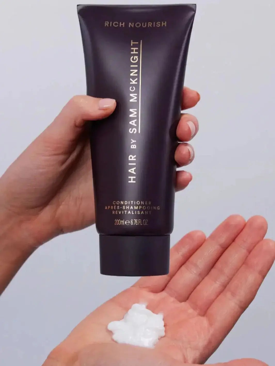 A hand squeezes a dollop of thick white product out of a dark purple squeeze tube of Hair by Sam McKnight Rich Nourishing Conditioner | Twentyseven Toronto