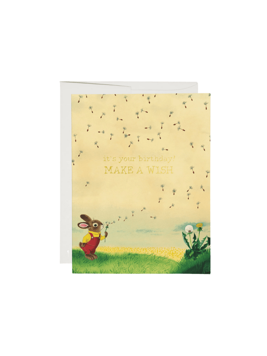 A Red Cap Cards Bunny and Dandelion Greeting Card by Richard Scarry features an illustrated little rabbit in overalls blowing dandelion seeds into the air next to a white envelope | Twentyseven Toronto