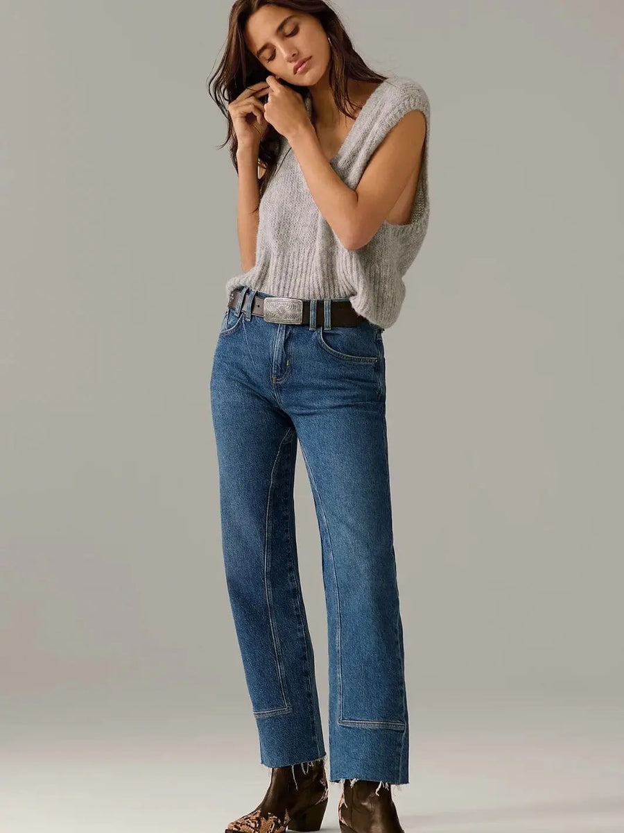 A model wearing the straight-leg Free People Risk Taker Mid-Rise Jeans - Be Bold styled with a grey knit vest, a large western belt buckle, and snakeskin boots | Twentyseven Toronto