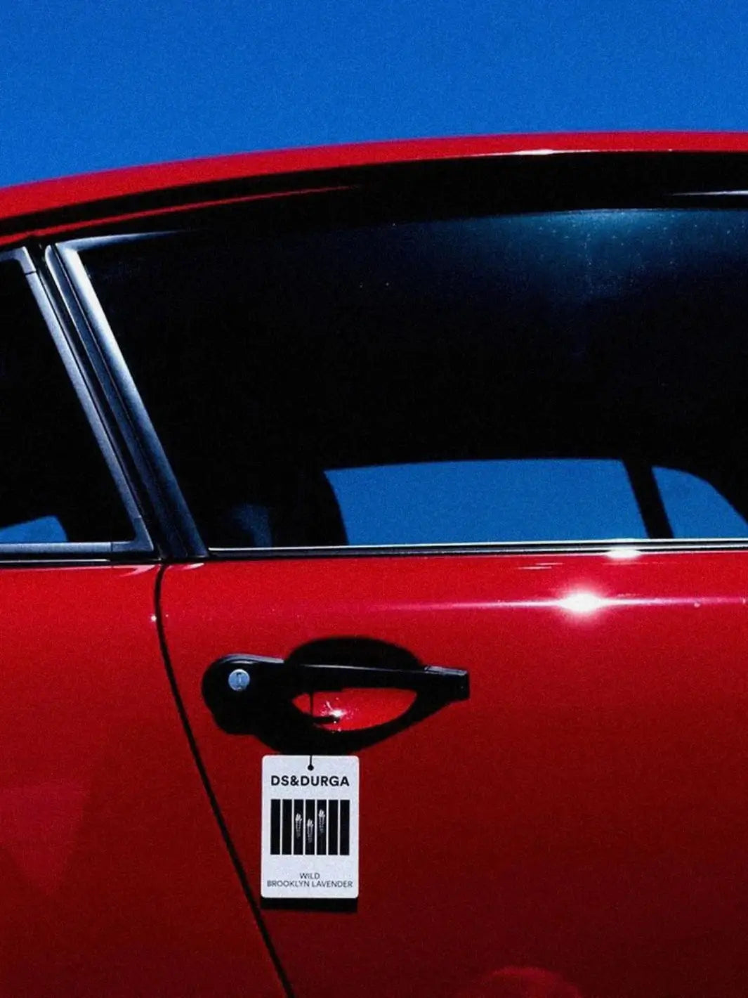 Red car with a DS&Durga air freshener tag against a blue background | Twentyseven Toronto