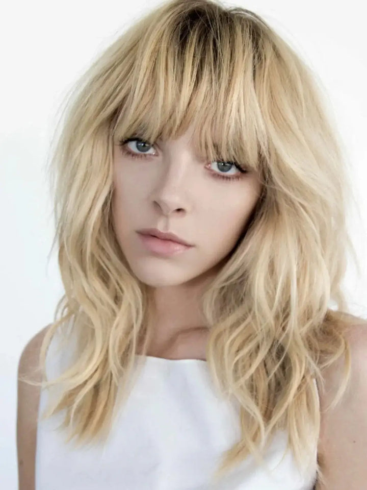 A model with blonde hair showcases piecey, beachy waves and full bangs styled with R+Co ROCKAWAY Salt Spray | Twentyseven Toronto