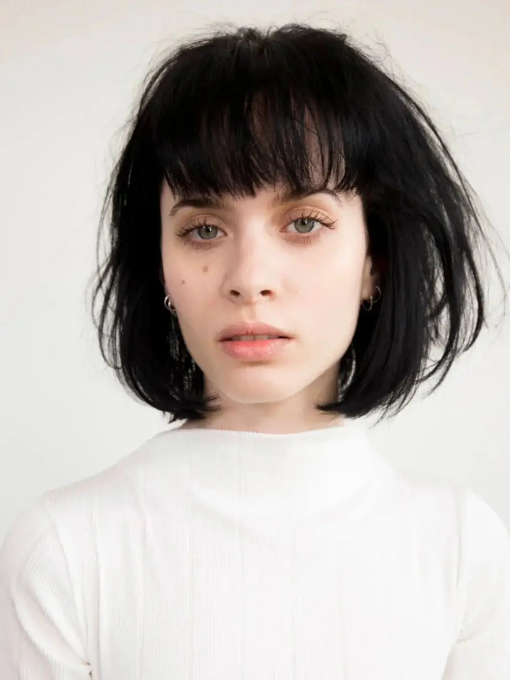 A front-facing headshot of a model with a thick, dark bob haircut and bangs styled with R+Co RODEO STAR Thickening Style Foam | Twentyseven Toronto