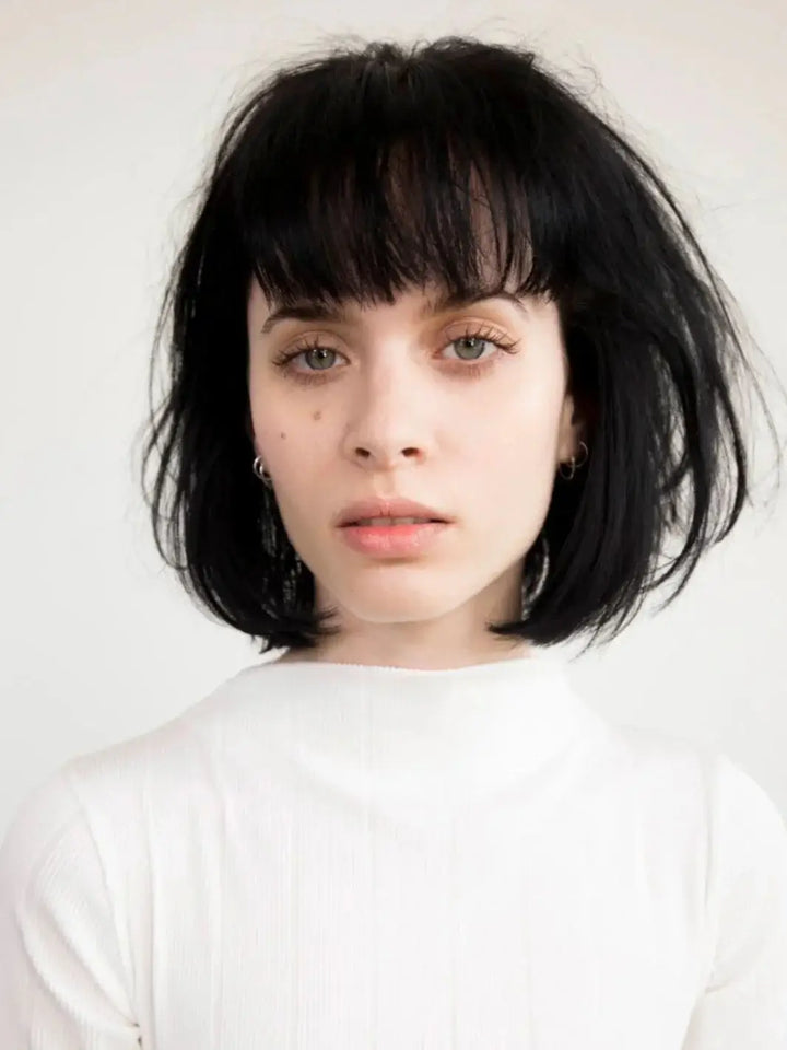 A front-facing headshot of a model with a thick, dark bob haircut and bangs styled with R+Co RODEO STAR Thickening Style Foam | Twentyseven Toronto