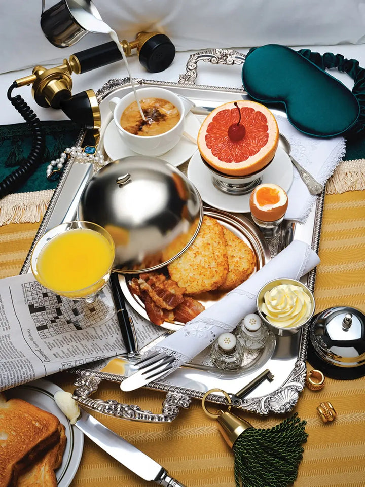 A lavish breakfast tray filled with hash browns, bacon, orange juice, a soft-boiled egg, and a grapefruit half forms the decadent scene for the Piecework Puzzles Room Service 1000 Piece Puzzle | Twentyseven Toronto