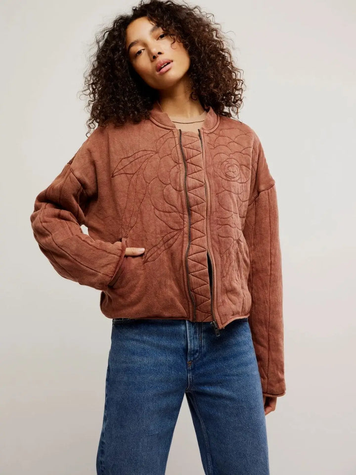 A model poses from the front to showcase the relaxed bomber jacket fit, ribbed collar, and warm reddish-brown hue of the Free People Rose Zip-Up Sweatshirt - Cinnamon Stick | Twentyseven Toronto
