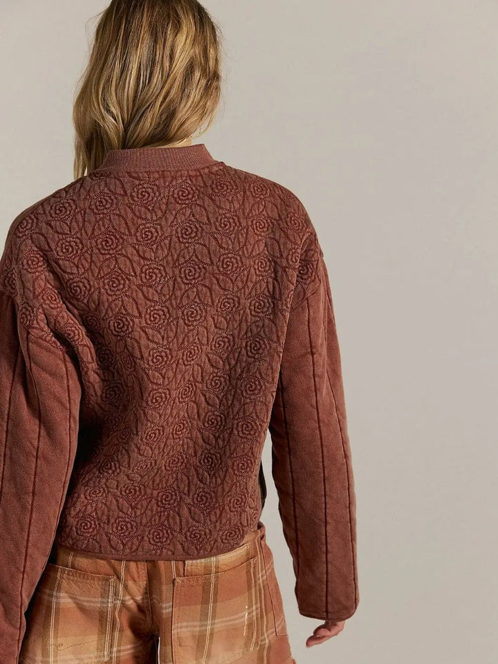 A rear view focuses on the repeating quilted floral pattern across the upper back and shoulders of the Free People Rose Zip-Up Sweatshirt - Cinnamon Stick | Twentyseven Toronto