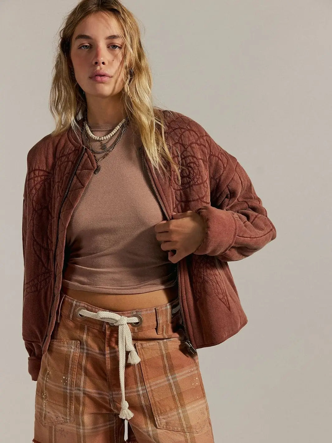 A model wears the unzipped Free People Rose Zip-Up Sweatshirt - Cinnamon Stick layered over a beige top and paired with plaid trousers | Twentyseven Toronto