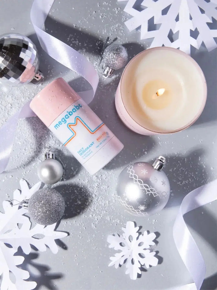 A top-down view captures a lit pink jar candle arranged amidst silver holiday ornaments, white paper snowflakes, and scattered faux snow to showcase the festive setting for the Mason Pearson Rosy Pits Scented Candle | Twentyseven Toronto