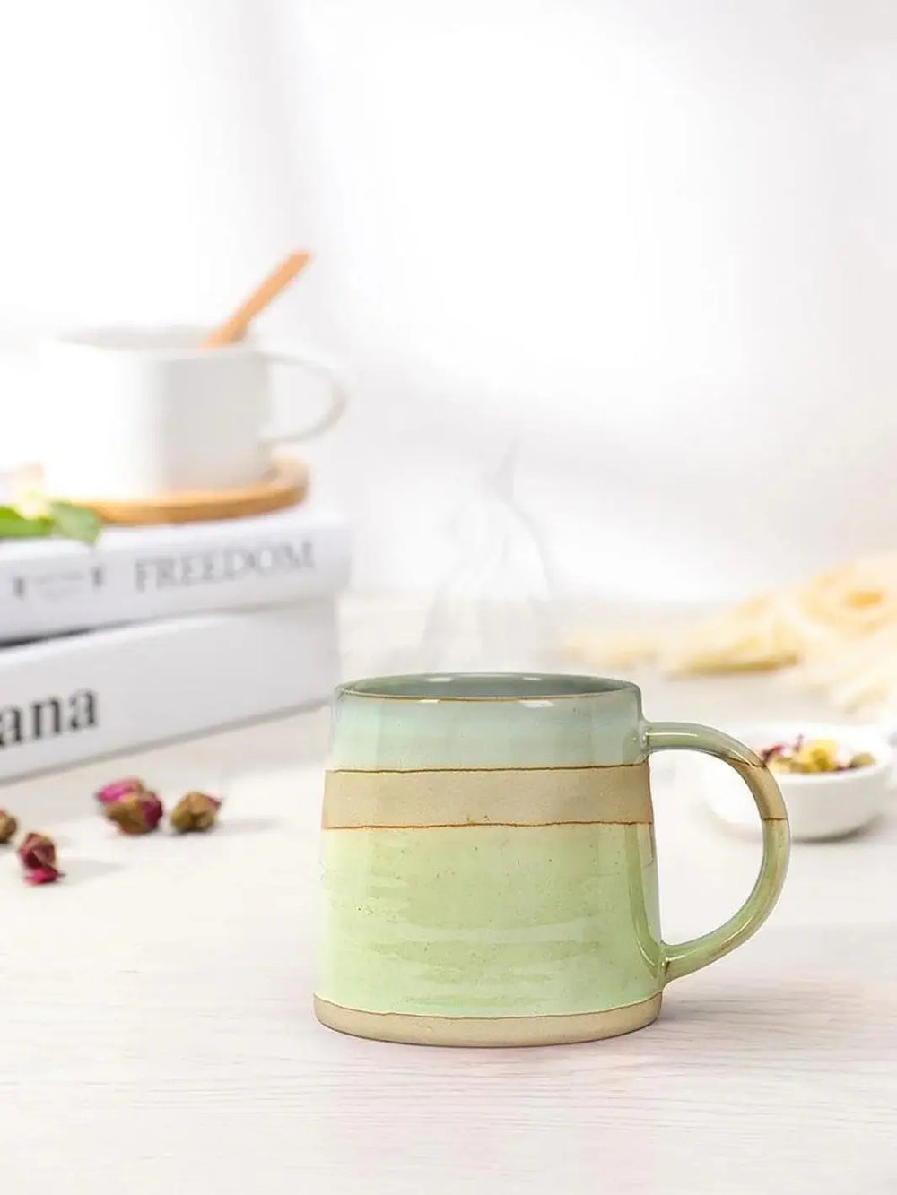 A blue, green and pink Abbott Collection Rustic Style Mug sits on a white tabletop surrounded by dried rosebuds and stacked decorative books | Twentyseven Toronto