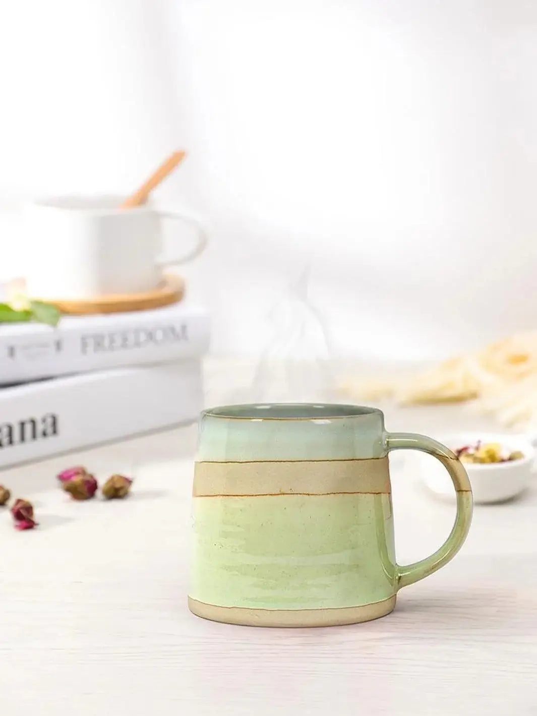 A blue, green and pink Abbott Collection Rustic Style Mug sits on a white tabletop surrounded by dried rosebuds and stacked decorative books | Twentyseven Toronto