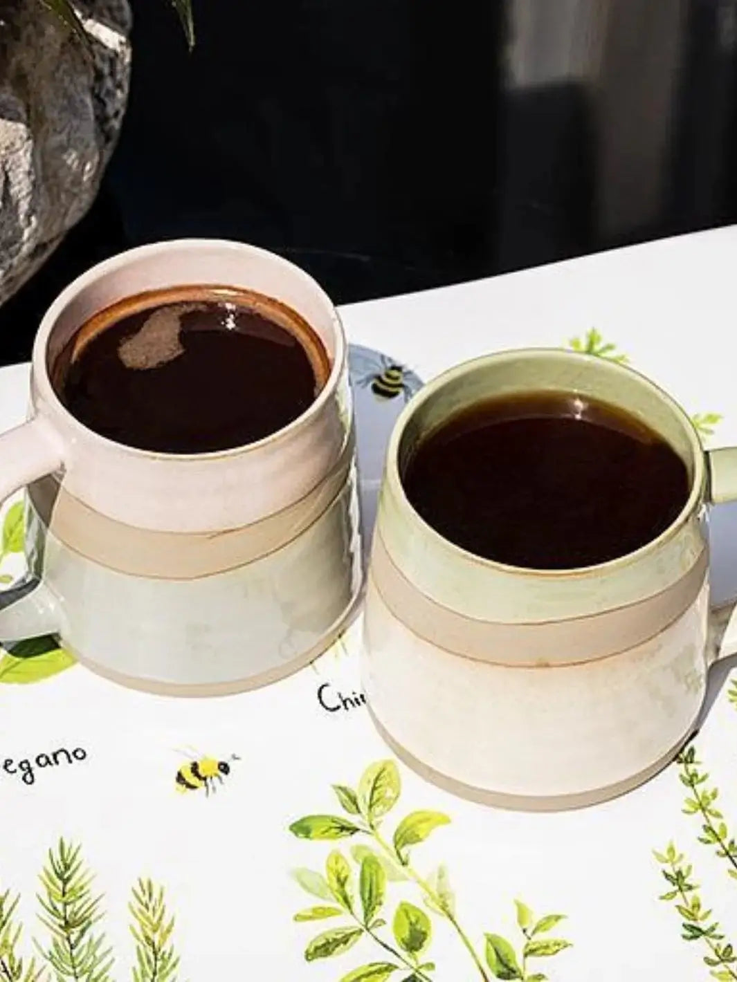 A high-angle close-up showcases two ceramic mugs filled with black coffee on a leaf-patterned surface, highlighting the Abbott Collection Rustic Style Mugs | Twentyseven Toronto