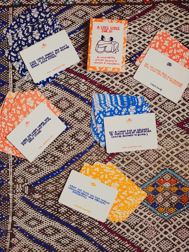 Several prompt cards from the A Safe Space For Us Deck from People I've Loved are arranged face-up on a patterned rug to display different vulnerability questions | Twentyseven Toronto