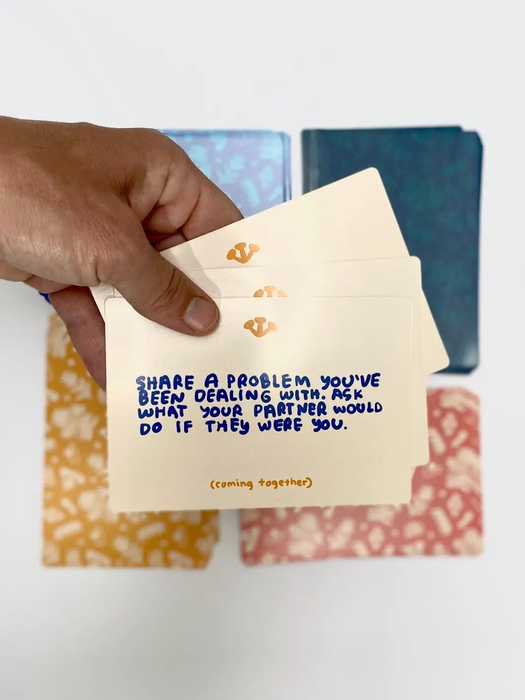 A hand displays a prompt card reading "Share a problem you've been dealing with..." from the "(coming together)" section of the A Safe Space For Us Deck from People I've Loved | Twentyseven Toronto