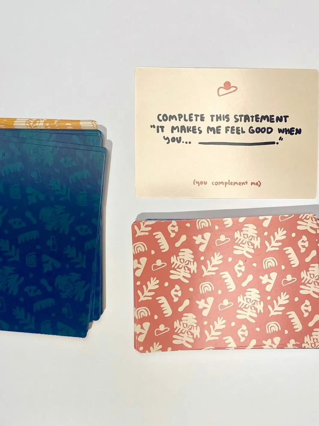 A prompt card from the "(you complement me)" section lies face up next to stacks of patterned cards from the A Safe Space For Us Deck from People I've Loved | Twentyseven Toronto