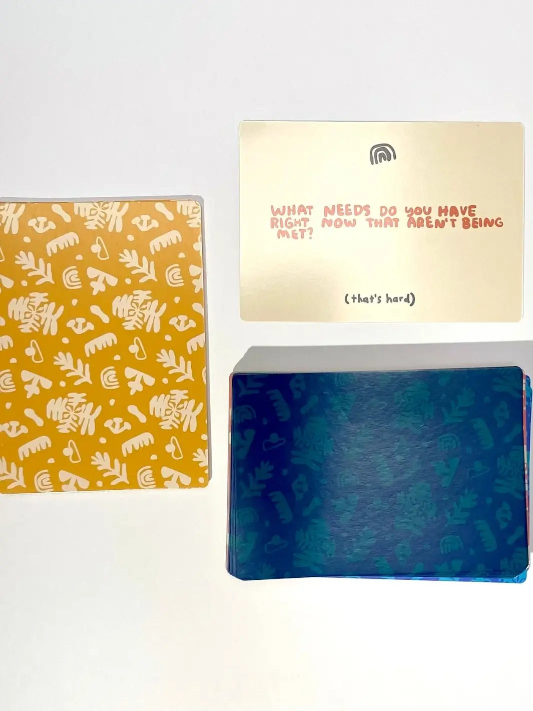 A card asking "What needs do you have right now that aren't being met?" is shown next to the distinctive yellow-patterned card back from the A Safe Space For Us Deck from People I've Loved | Twentyseven Toronto