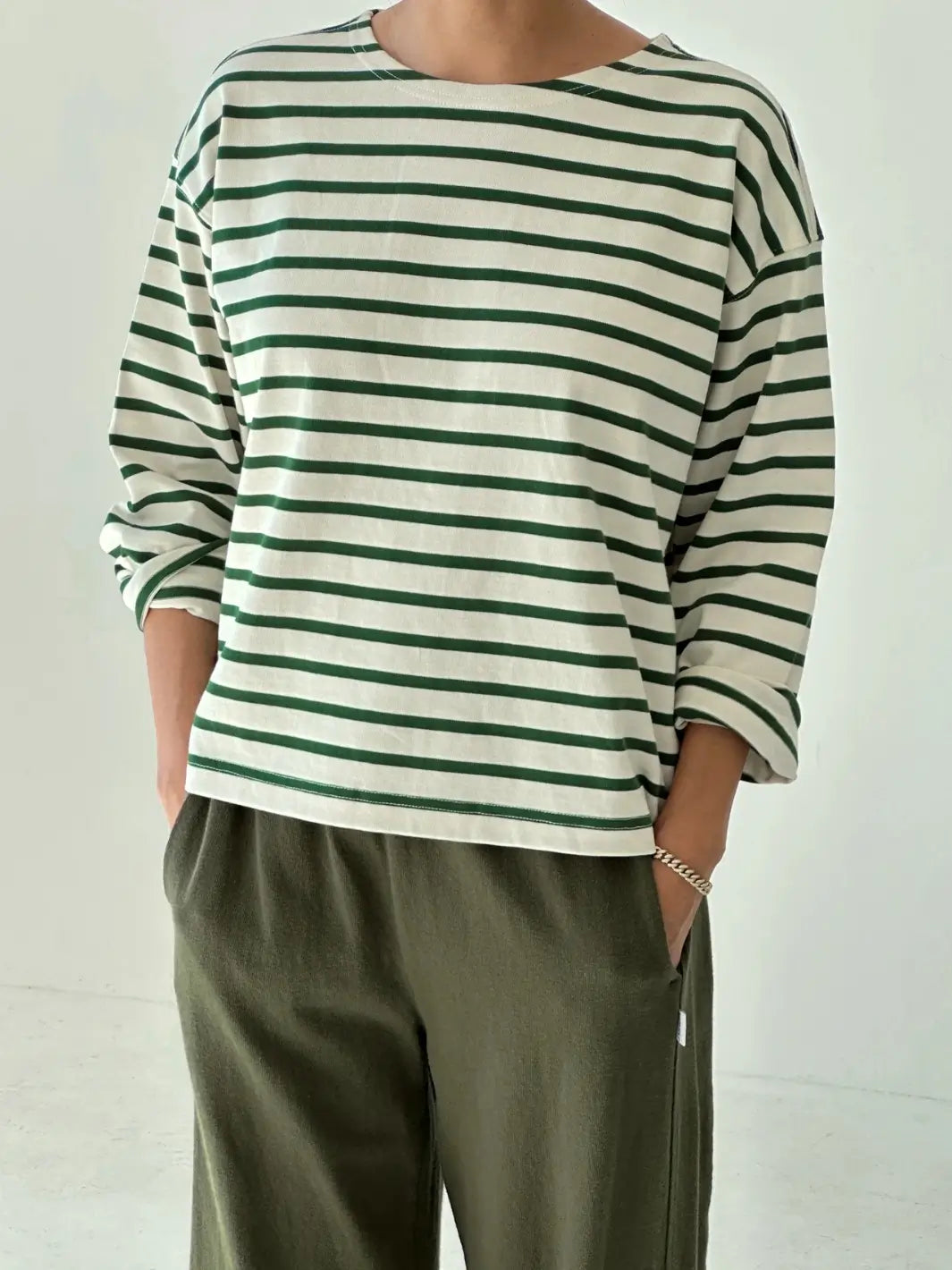 Person wearing a green and white striped 'Sailor Top' long sleeve shirt in 'Pine Stripe' with green pants from Le Bon Shoppe on a white background | Twentyseven Toronto