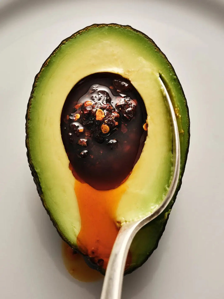 A close-up view of an avocado half filled with rich, oil-rich Flamingo Estate Salsa Macha Chile Crisp | Twentyseven