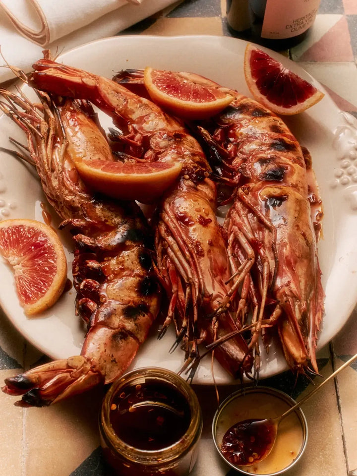 Plated grilled prawns garnished with blood orange slices alongside a jar and dish of Flamingo Estate Salsa Macha Chile Crisp | Twentyseven