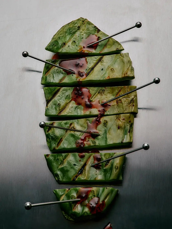 Grilled nopales cactus slices arranged in a row with metal picks and drizzled with spicy Flamingo Estate Salsa Macha Chile Crisp | Twentyseven