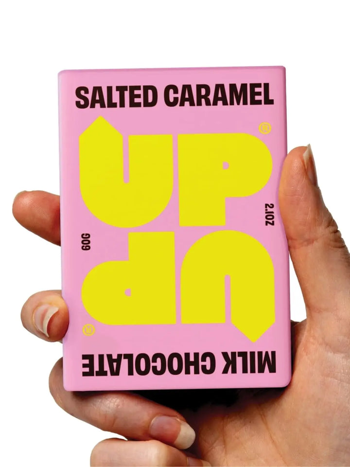 Hand holding an UP UP Chocolate Salted Caramel Milk Chocolate bar in pink and yellow packaging | Twentyseven Toronto