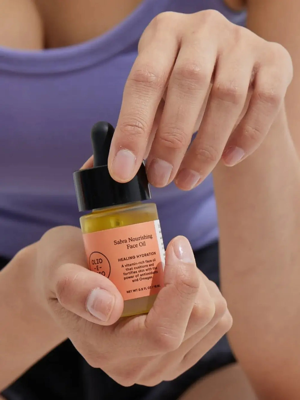 Person in purple shirt holding Olio E Ossi Salva Nourishing Face Oil dropper bottle | Twentyseven Toronto