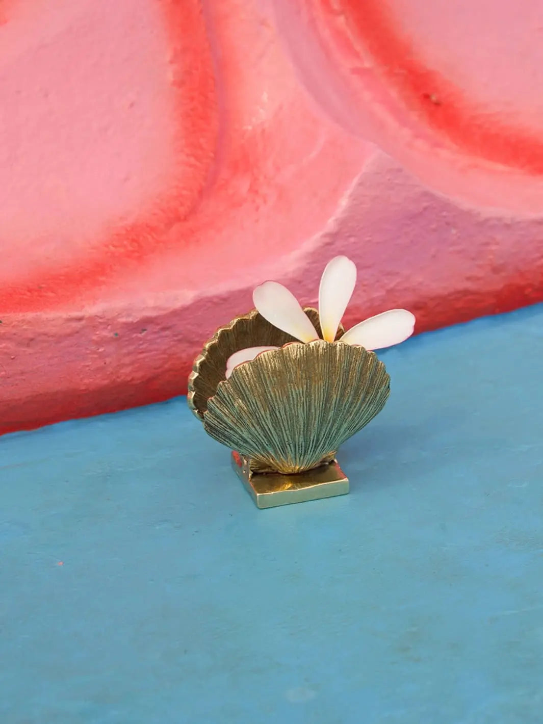 Gold decorative shell holder by Doing Goods holding a flower on a blue and pink background | Twentyseven Toronto