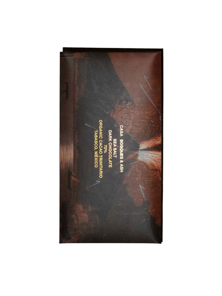 A vertical chocolate wrapper featuring a dramatic illustration of a volcanic eruption at night with gold text labeled 'Sea Salt 70% - Ash Chocolate Bar' from Casa Bosques | Twentyseven Toronto