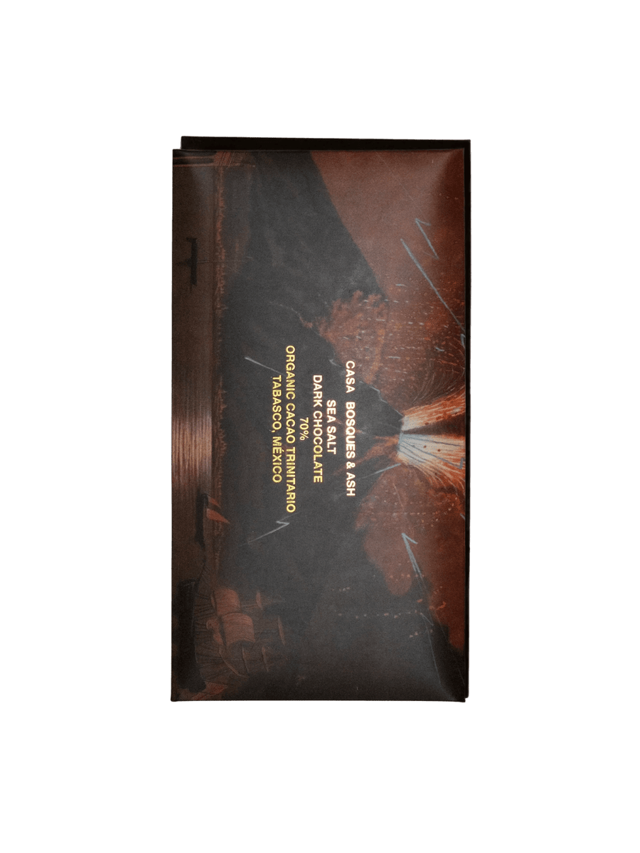 A vertical chocolate wrapper featuring a dramatic illustration of a volcanic eruption at night with gold text labeled 'Sea Salt 70% - Ash Chocolate Bar' from Casa Bosques | Twentyseven Toronto