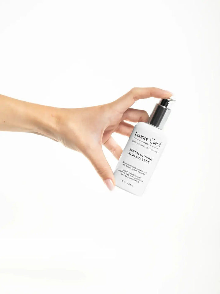 Hand holding a bottle of Leonor Greyl 'Serum de Soie Sublimateur' against a white background | Twentyseven Toronto