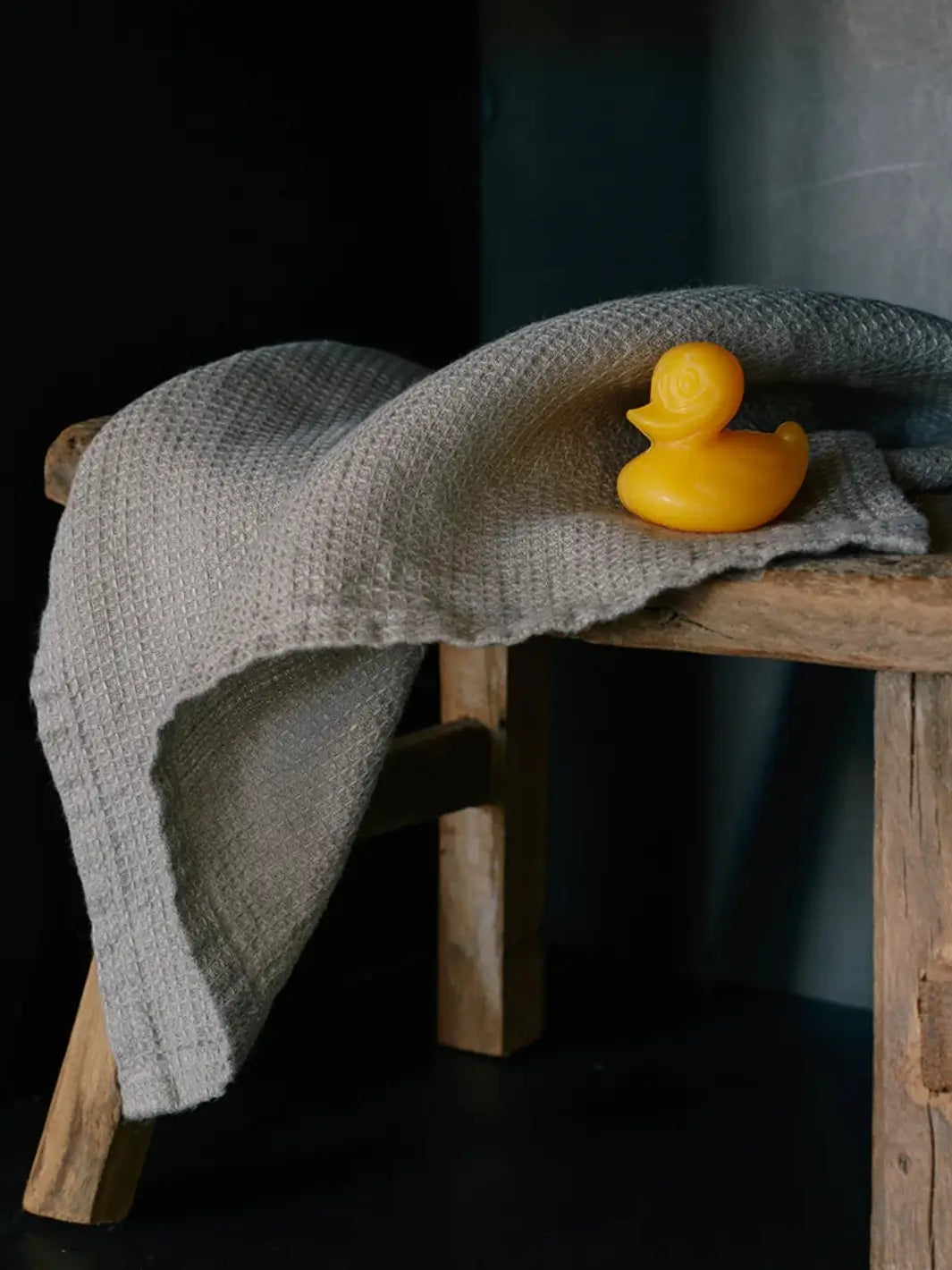 Yellow Sheep's Milk Soap in 'Duckling' from Burstenhaus Redecker on a gray towel draped over a wooden stool against a dark background | Twentyseven Toronto