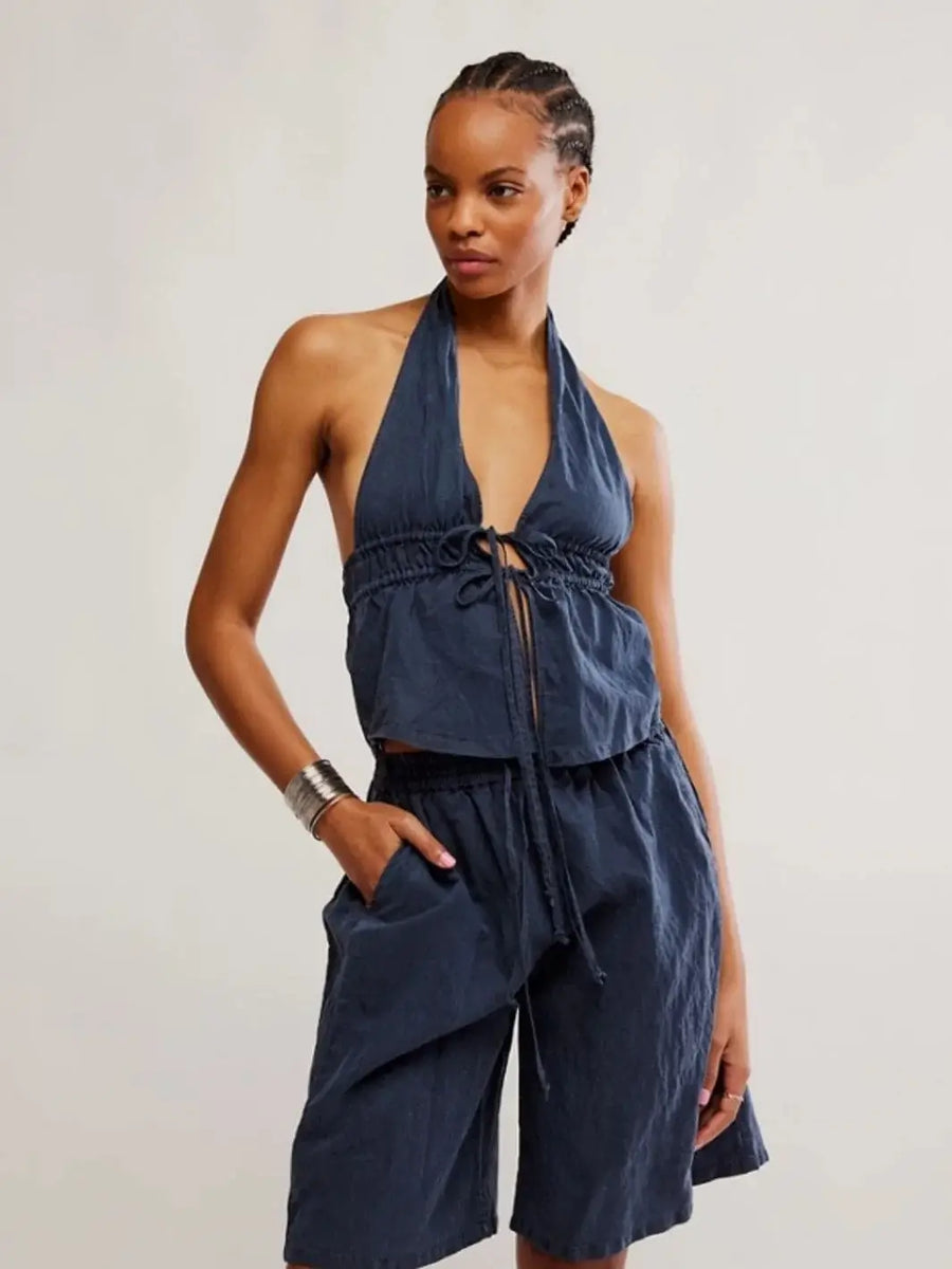 A model poses in a studio setting wearing the dark navy Free People Sidra Set - India Ink, featuring a halter-neck tie-front top and relaxed, matching drawstring shorts | Twentyseven Toronto