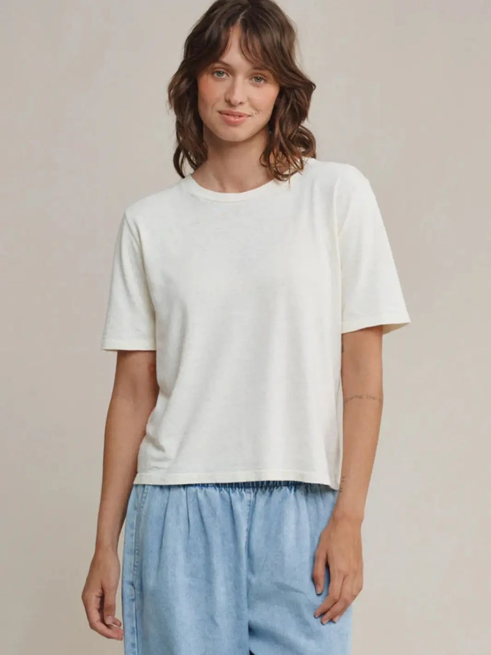 Front view of a brunette model posing in the off-white Jungmaven Silverlake Cropped Tee and light blue pants against a beige backdrop | Twentyseven 