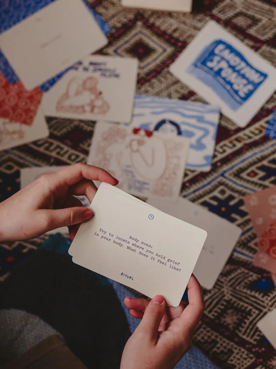 A pair of hands holds a prompt card from the Sitting With Sadness Deck from People I've Loved that encourages a body scan to locate where grief is held | Twentyseven Toronto