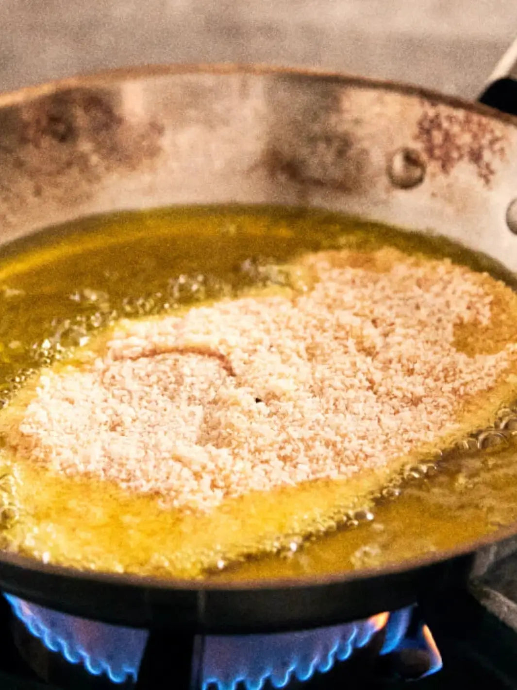 Fried food item in a pan with Graza 'Sizzle' oil on a stovetop | Twentyseven Toronto