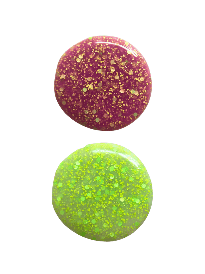 Two circular swatches of glittery 'Skunk Dreams' nail polish by Death Valley Nails, one pink and one green, on a transparent background | Twentyseven Toronto