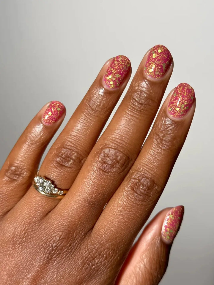 Hand with glittery pink nails, using 'Skunk Dreams' nail polish by Death Valley Nails and a diamond ring on a white background | Twentyseven Toronto