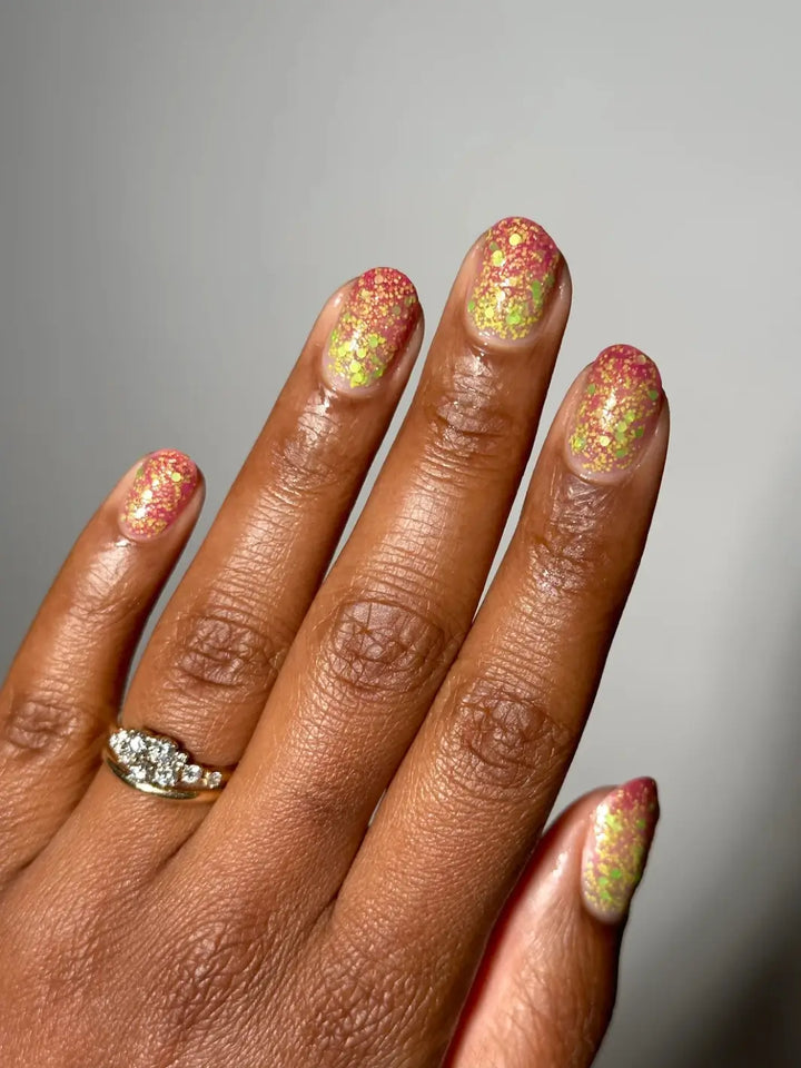 Hand with glittery pink and green nails, using 'Skunk Dreams' nail polish by Death Valley Nails on a white background | Twentyseven Toronto