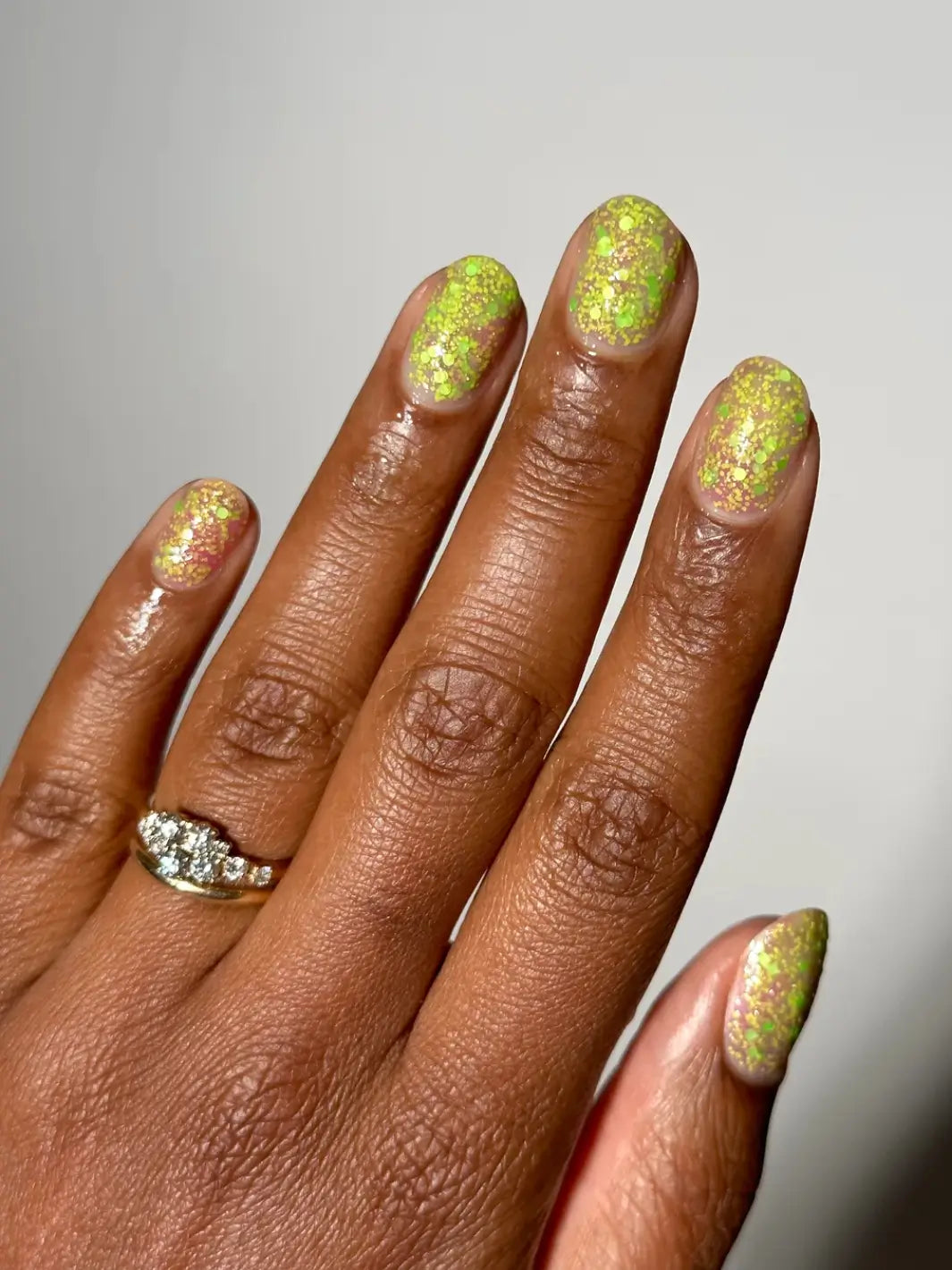 Hand with glittery green nails, using 'Skunk Dreams' nail polish by Death Valley Nails on a white background | Twentyseven Toronto