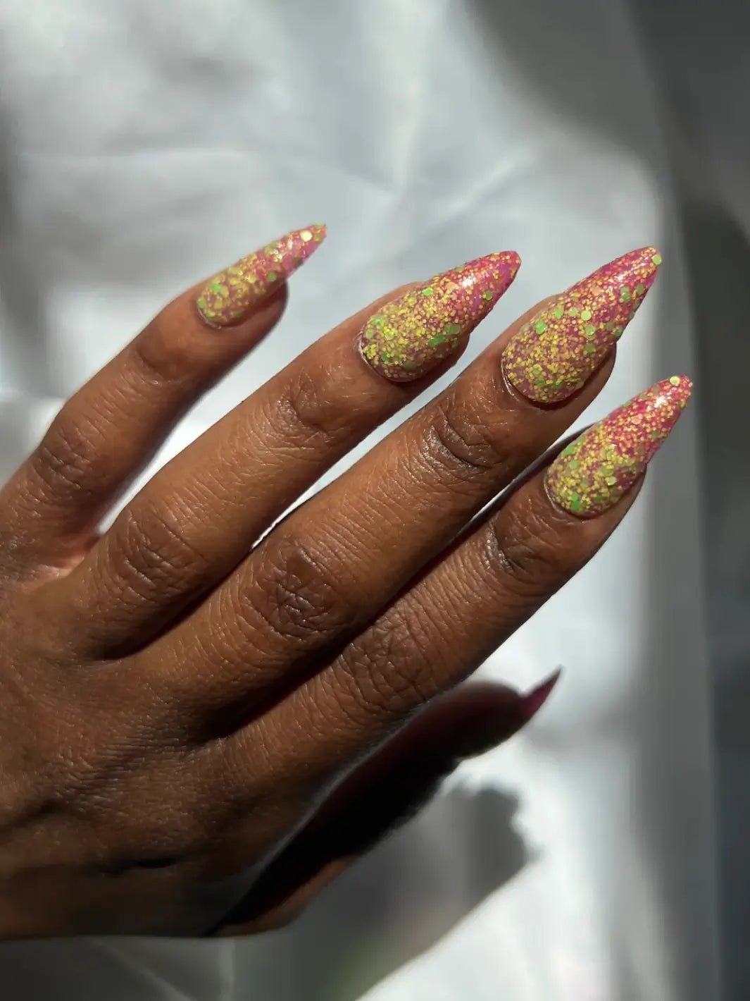 Hand with long glittery pink and green nails, using 'Skunk Dreams' nail polish by Death Valley Nails on a white background | Twentyseven Toronto