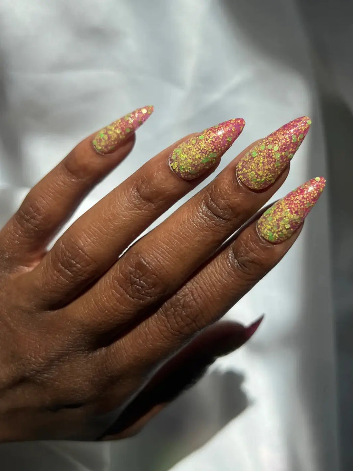 Hand with long glittery pink and green nails, using 'Skunk Dreams' nail polish by Death Valley Nails on a white background | Twentyseven Toronto