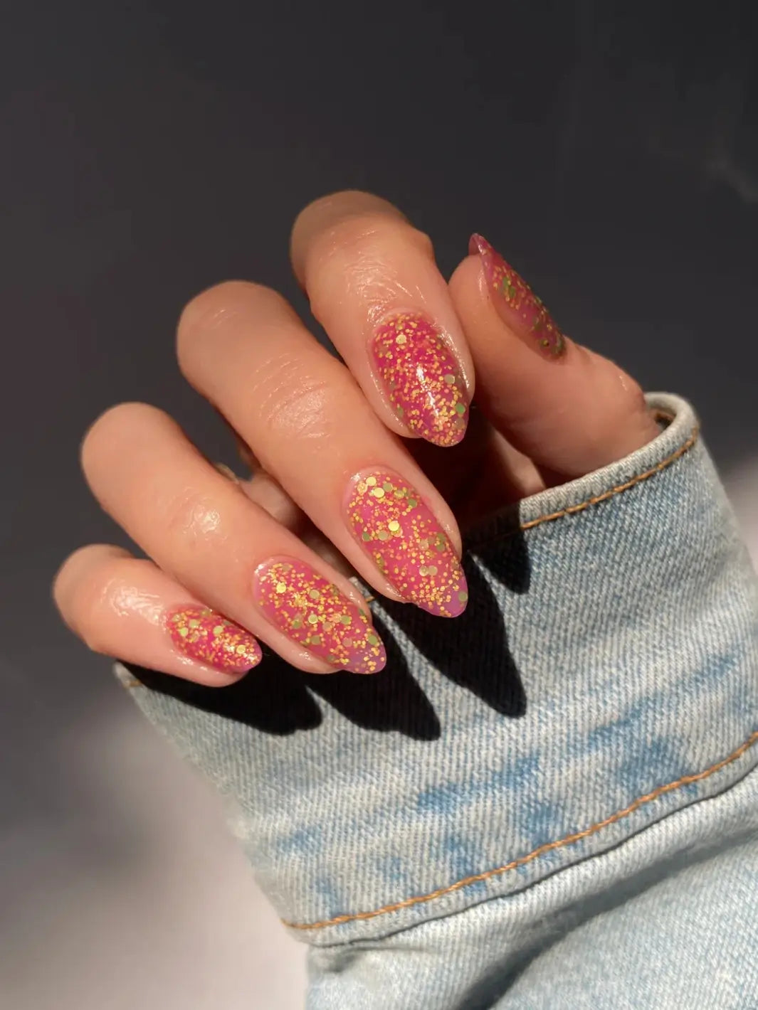 Hand with glittery pink nails, using 'Skunk Dreams' nail polish by Death Valley Nails on a dark background | Twentyseven Toronto