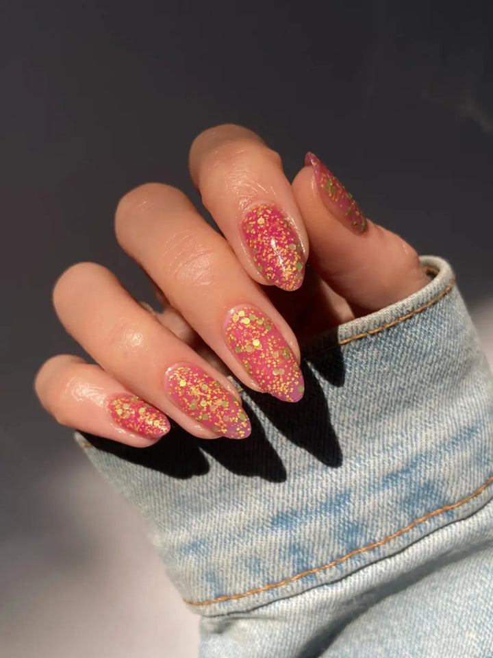 Hand with glittery pink nails, using 'Skunk Dreams' nail polish by Death Valley Nails on a dark background | Twentyseven Toronto