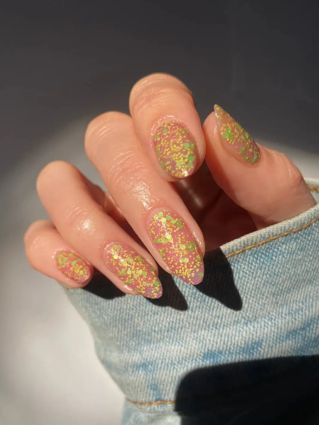 Hand with glittery pink and green nails, using 'Skunk Dreams' nail polish by Death Valley Nails on a white background | Twentyseven Toronto