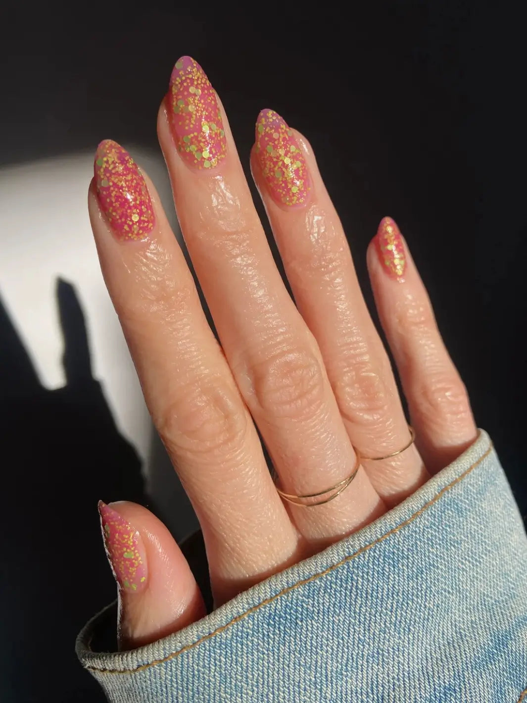 Hand with glittery pink and green nails, using 'Skunk Dreams' nail polish by Death Valley Nails on a dark background | Twentyseven Toronto