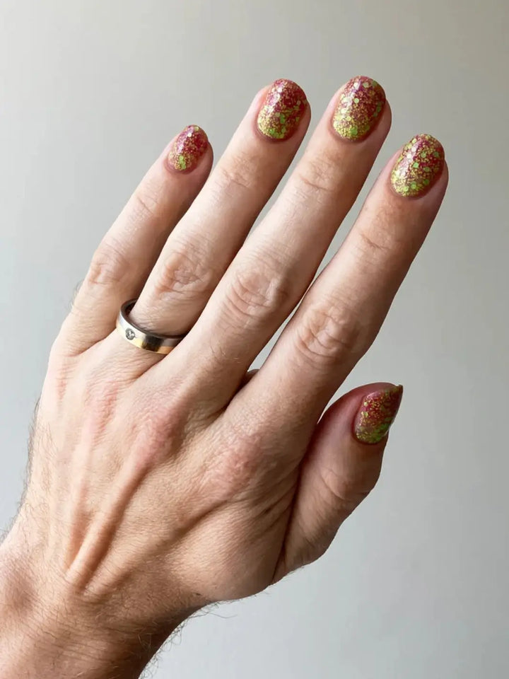 Hand with glittery pink and green nails, using 'Skunk Dreams' nail polish by Death Valley Nails on a white background | Twentyseven Toronto