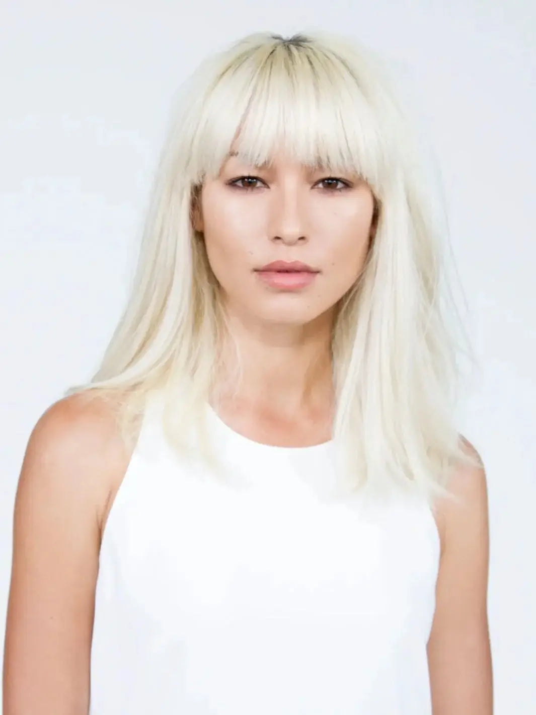 A model with straight, bright blonde hair and full bangs showcases a clean, matte texture styled with R+Co SKYLINE Dry Shampoo Powder | Twentyseven Toronto