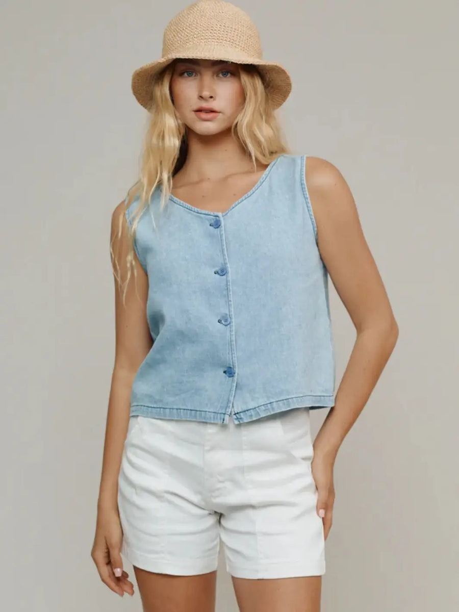 A model from the waist up showcases the v-neck and button-down front of the Jungmaven Skyline Summer Denim Vest - Light styled with white shorts and a straw hat | Twentyseven Toronto