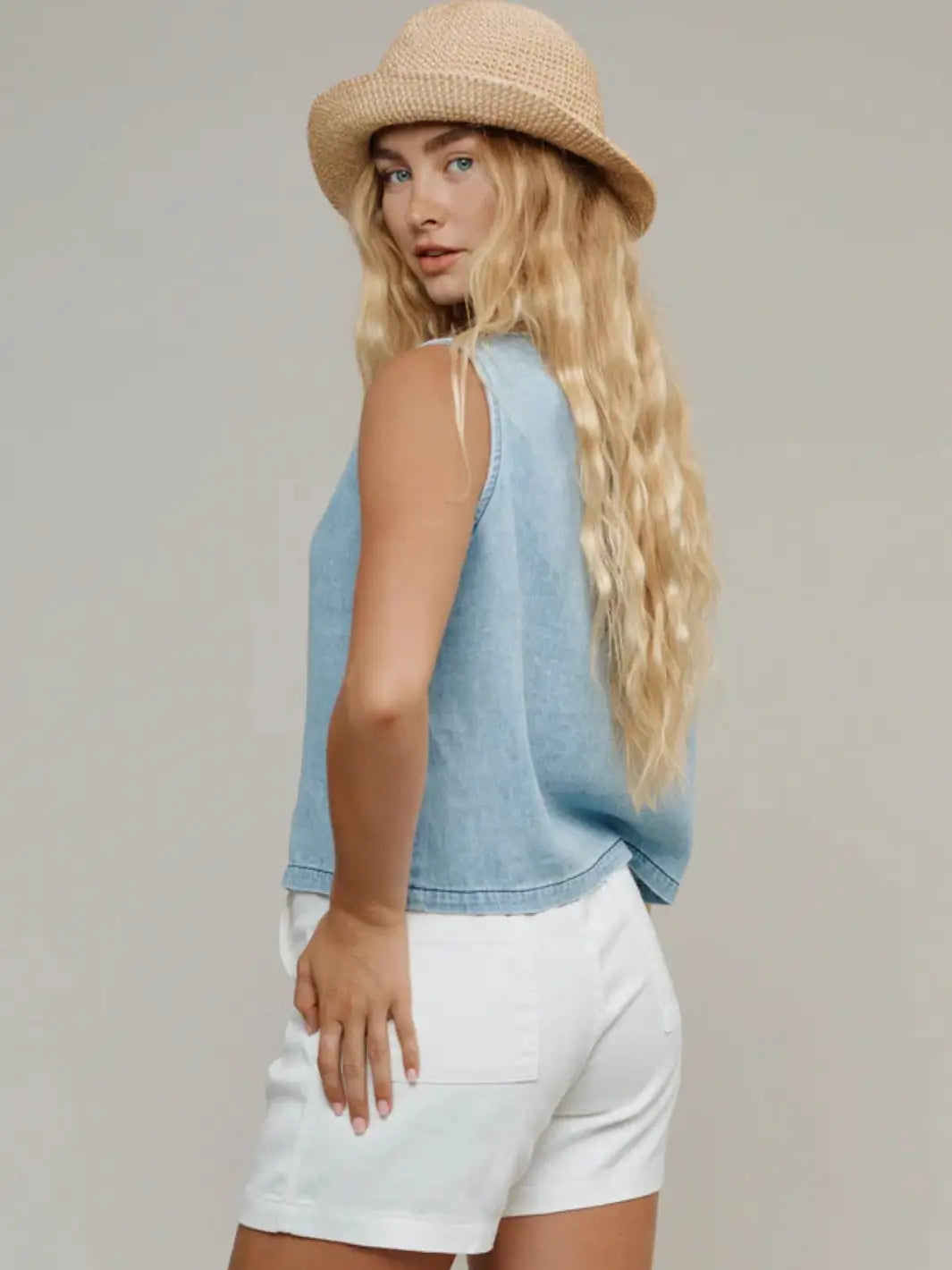 A model looks over her shoulder to show the back view and sleeveless silhouette of the Jungmaven Skyline Summer Denim Vest - Light | Twentyseven Toronto